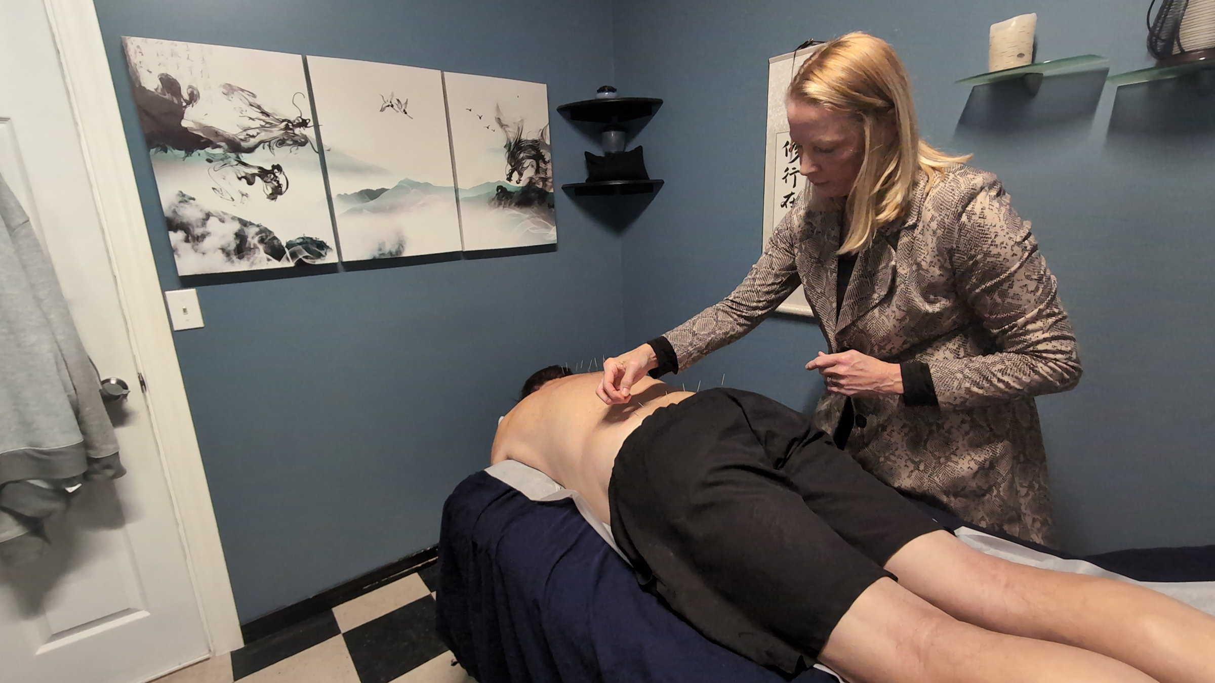 Acupuncturist Patty Kuchar, placing needles on the back of a male patient laying on the patient bed with his back skin exposed wearing black shorts.